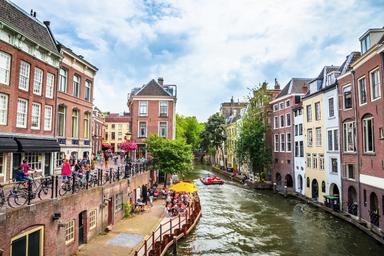 Il Vecchio Canale di Utrecht con i suoi caratteristici bar e locali a bordo fiume. Una piccola imbarcazione rossa sta raggiungendo il tendone giallo in basso