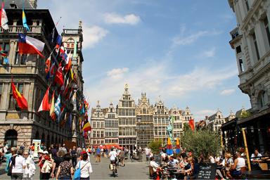 Piazza popolata di persone nella capitale del Belgio, Bruxelles. Delle bandiere sventolano dagli edifici di sinistra