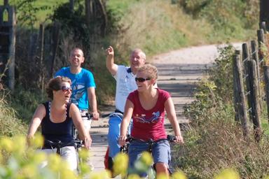 Quattro persone sorridenti pedalano sulla pista ciclabile. Uno di loro indica qualcosa che hanno di fronte