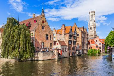 Casette e campanile lungo uno dei canali di Bruges con salice piangente sulla sinistra