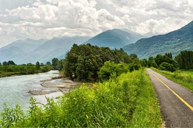 Il Sentiero della Valtellina a destra, segue il percorso del fiume Adda. In una giornata nuvolosa le montagne dominano il paesaggio